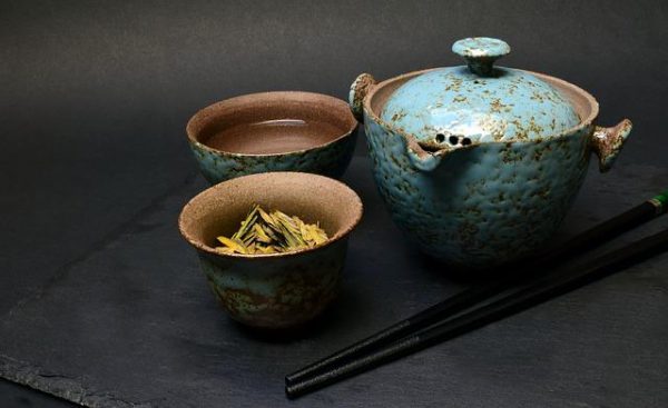 gliniany czajnik z dwoma filiżankami do zaparzania herbaty, w jednej z filiżanek znajduje się susz herbaciany