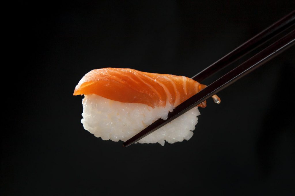 pałeczki trzymają sushi z ryżu i wędzonego łososia