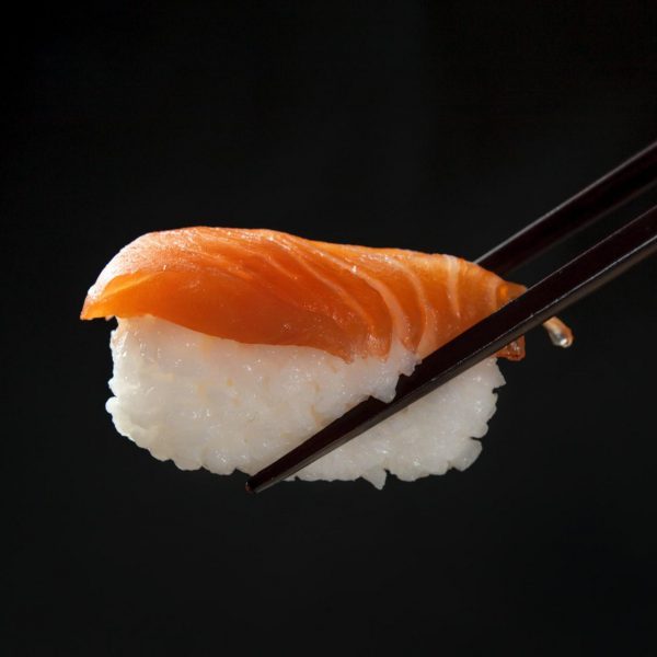 pałeczki trzymają sushi z ryżu i wędzonego łososia
