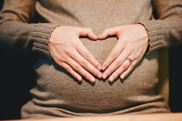 kobieta w ciąży ma ułożone dłonie w kształcie serca na brzuchu