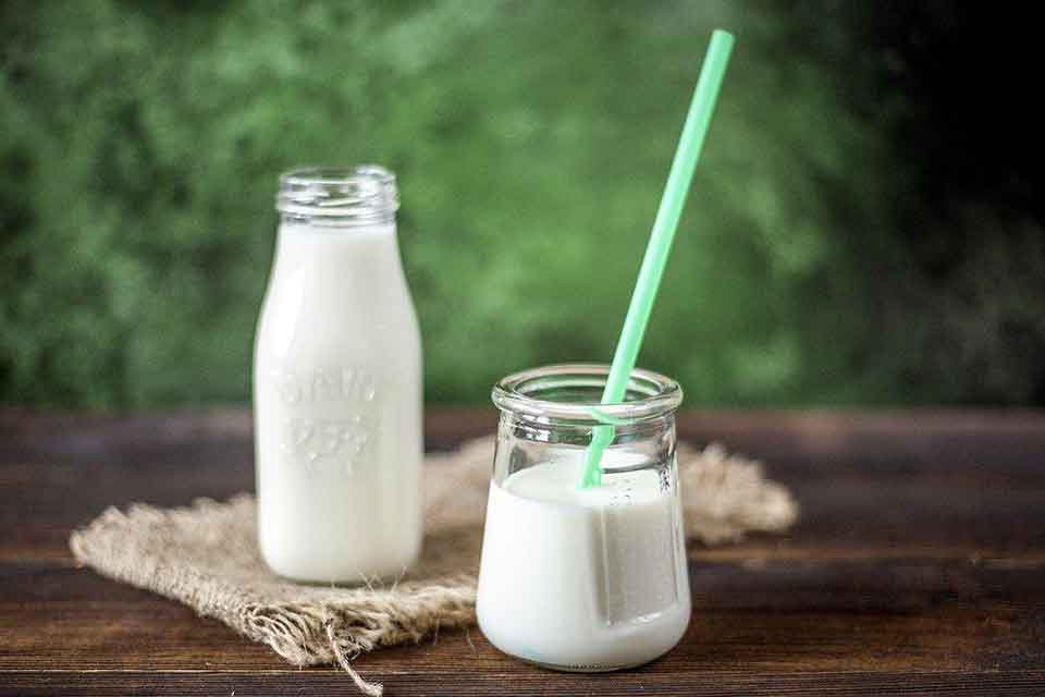 butelka z mlekiem a przed nią szklanka pełna mleka ze słomką