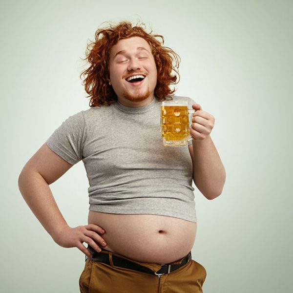 Uśmiechnięty mężczyzna z piwem w ręku ma odsłonięty brzuch piwny