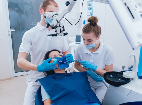 Stomatolog wykonuje leczenie kanałowe zęba, który boli kobietę z wykorzystaniem mikroskopu